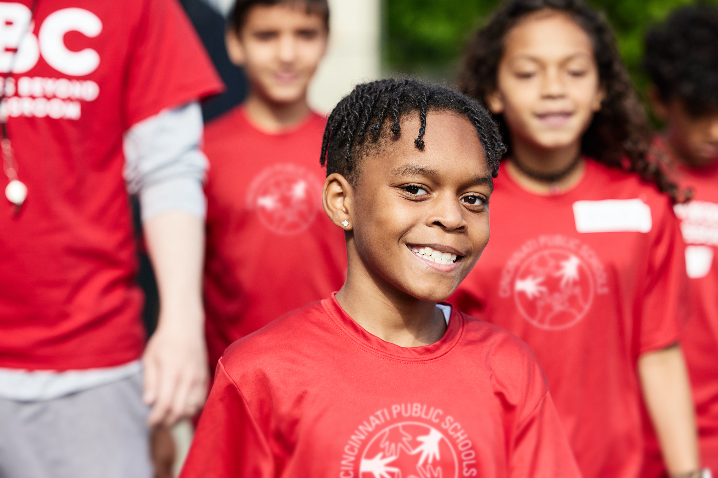 Smiling children in red shirts are outdoors, appearing joyful and engaged in an activity.