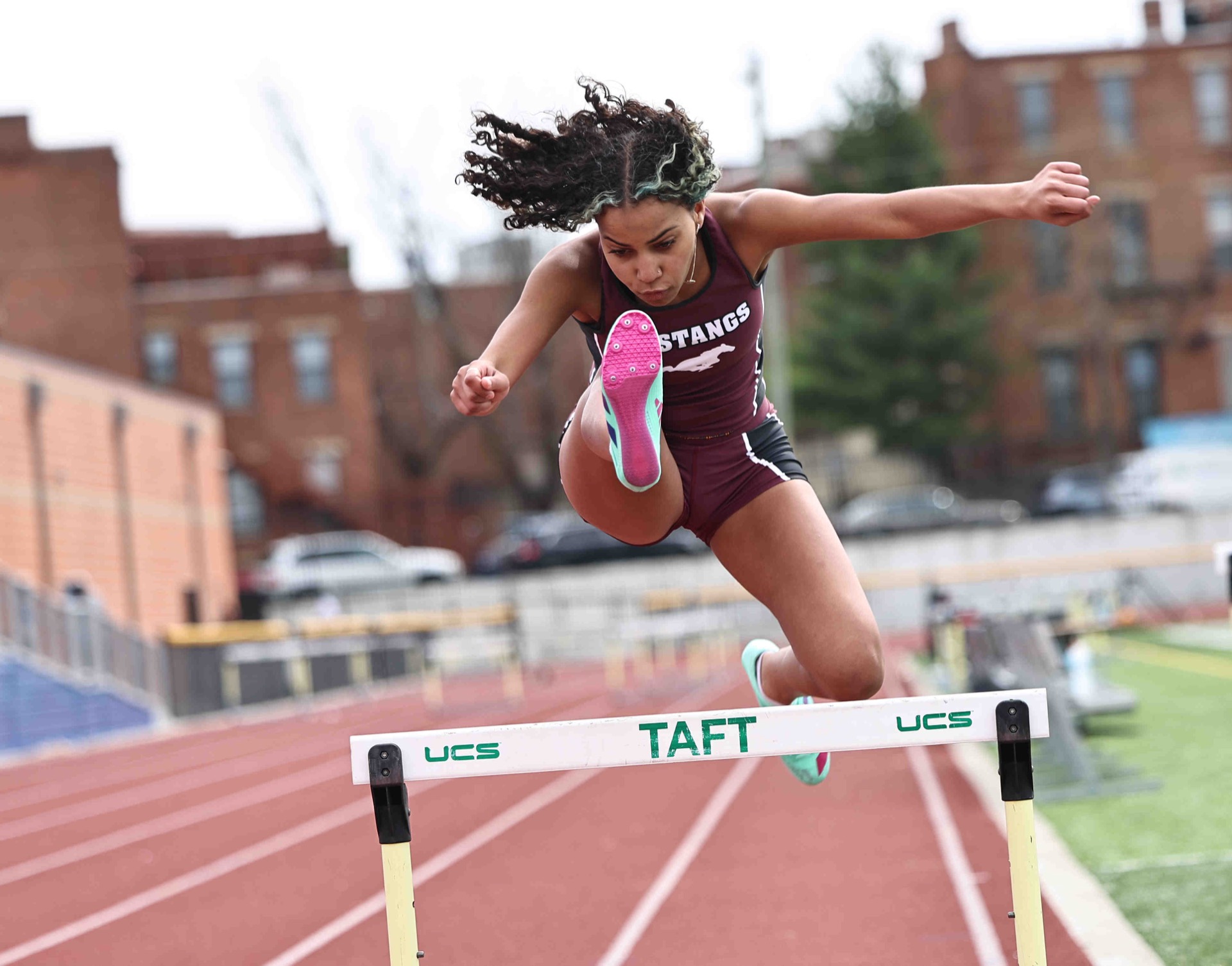 A track athlete is leaping over a hurdle on a race track.